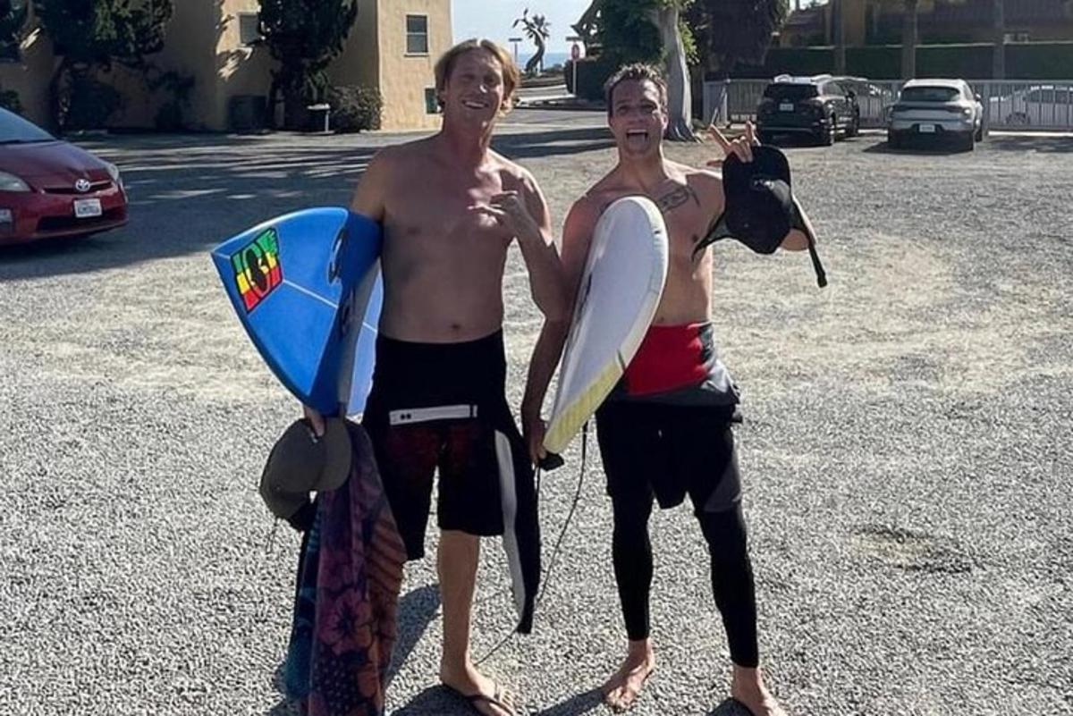 Δύο άντρες στέκονται σε ένα πάρκινγκ κρατώντας σανίδες του σερφ