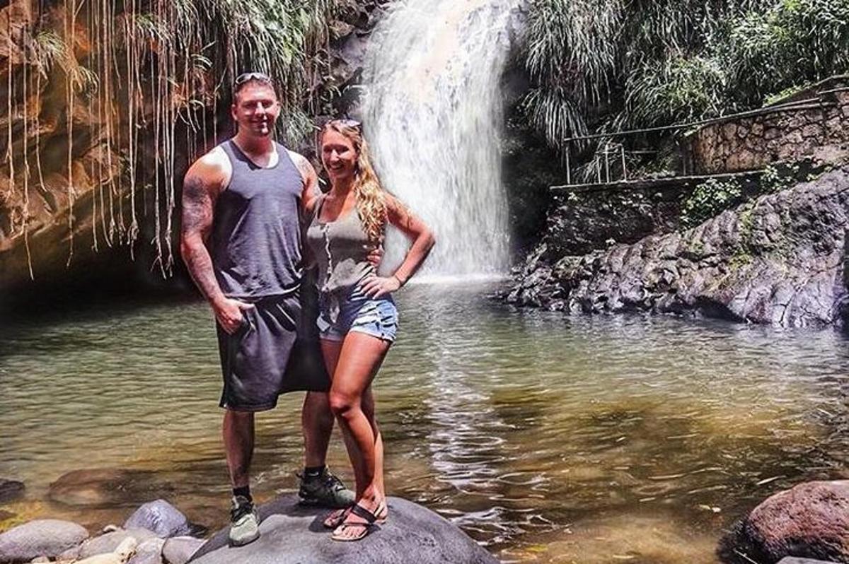 a man and woman standing on a rock in front of a waterfall