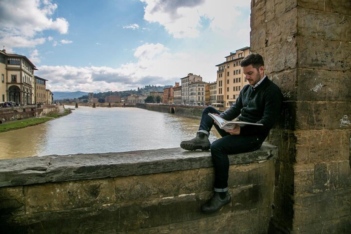 un home assegut a la paret llegint un llibre al costat d'un riu