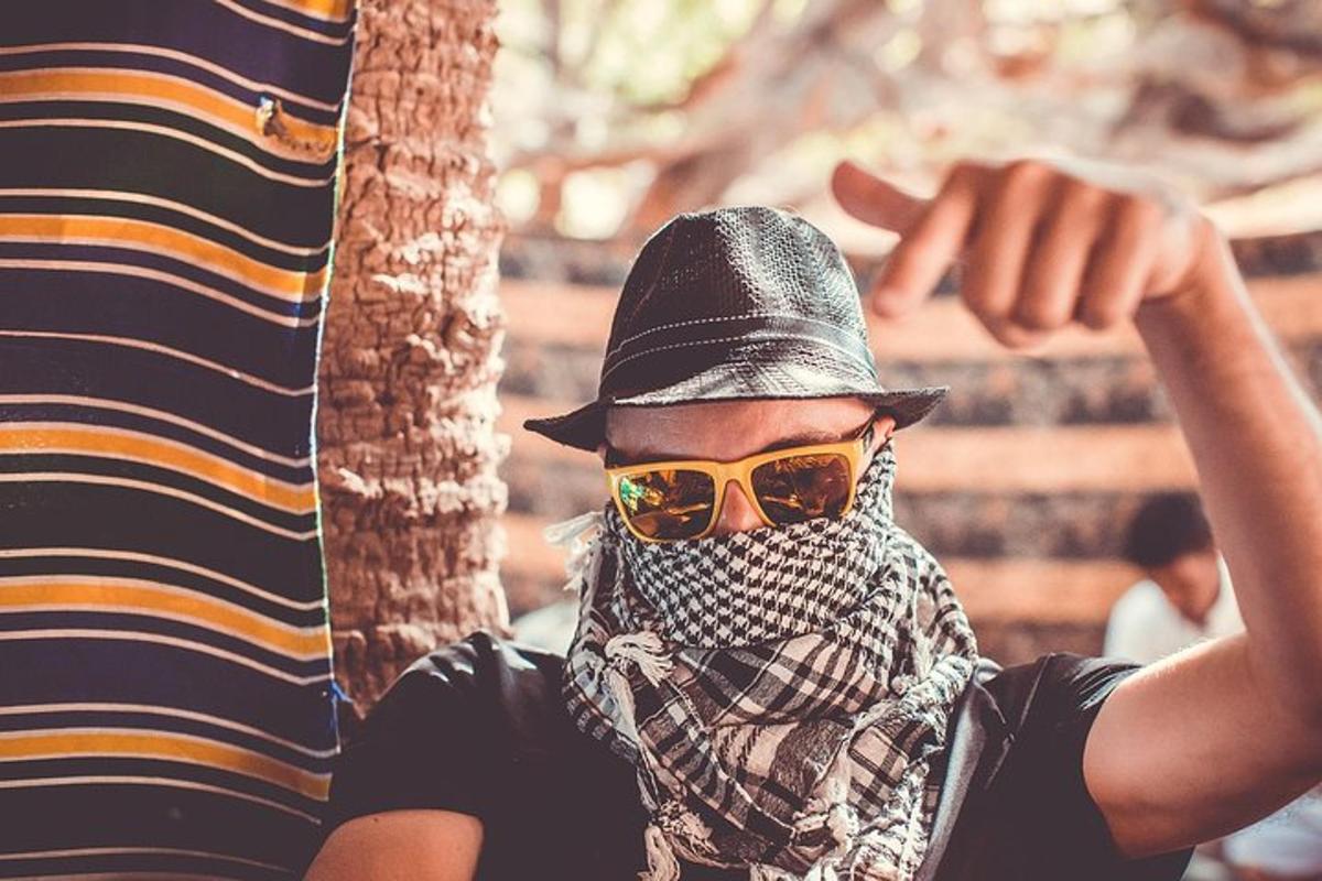 un uomo che indossa occhiali da sole, un cappello e una sciarpa