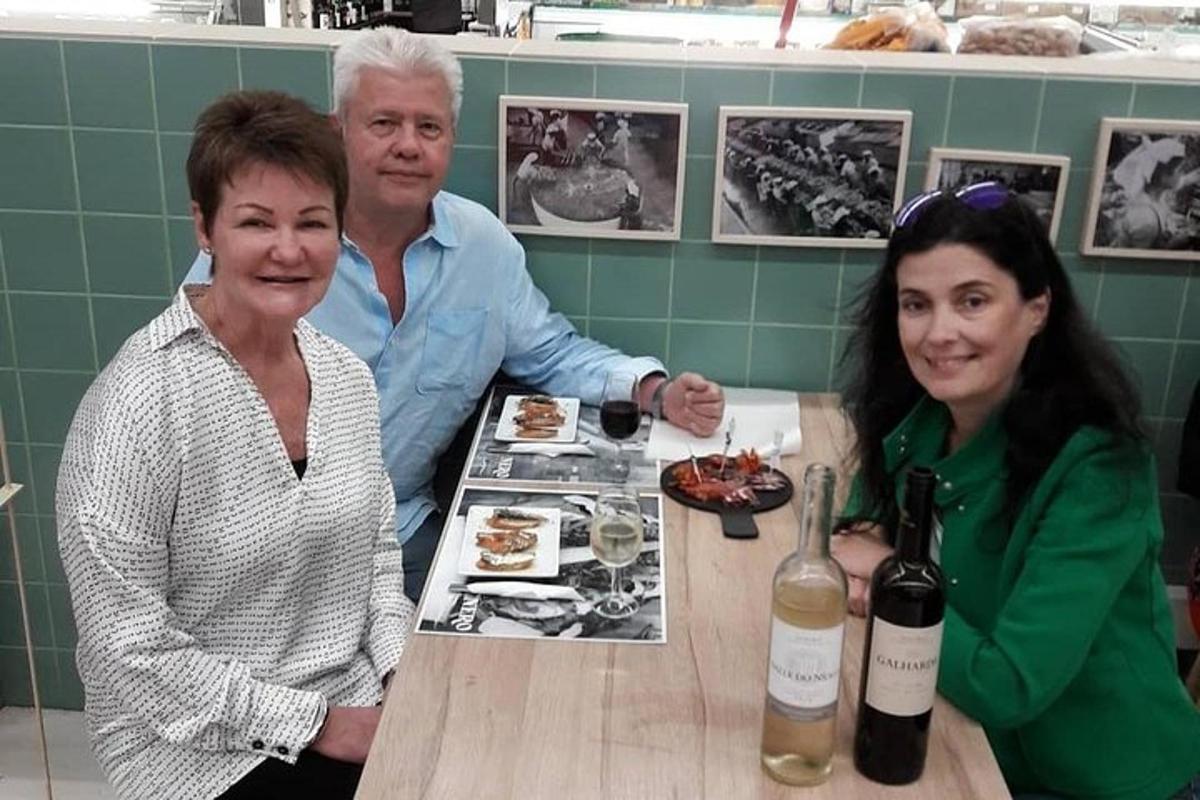 um homem e duas mulheres sentados à mesa com garrafas de vinho