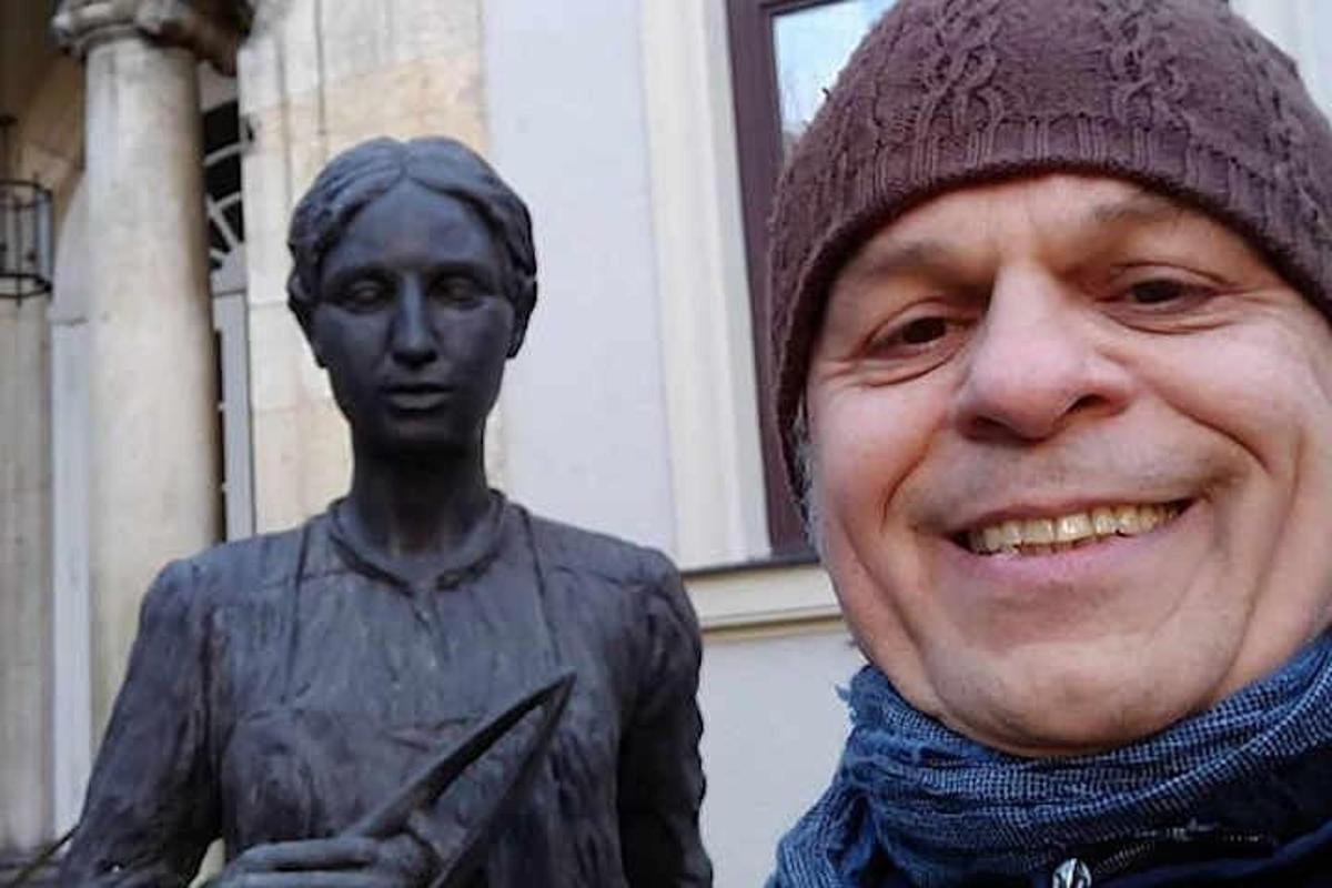 moški v klobuku stoji poleg kipa