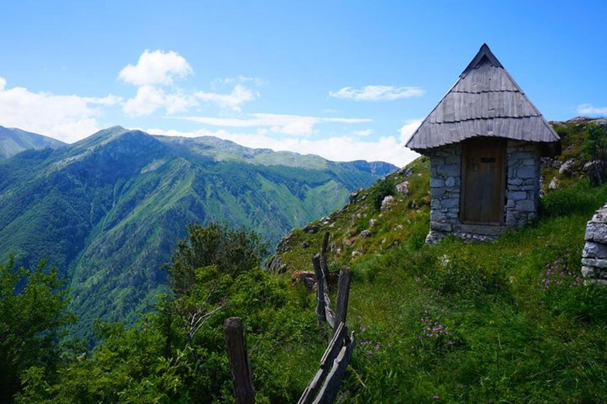 stara hiša na hribu z gorami v ozadju