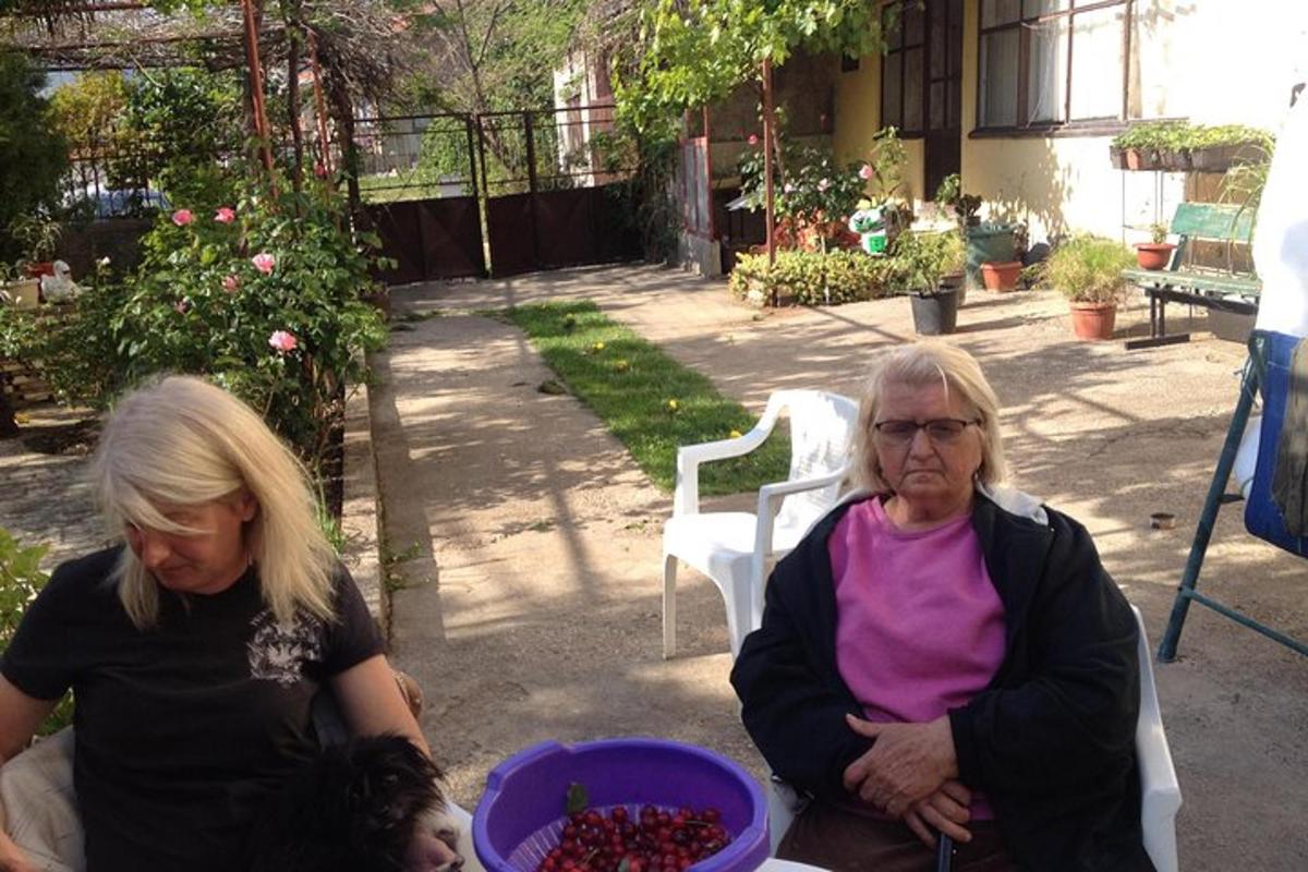 two women sitting on a table with a bowl of fruit
