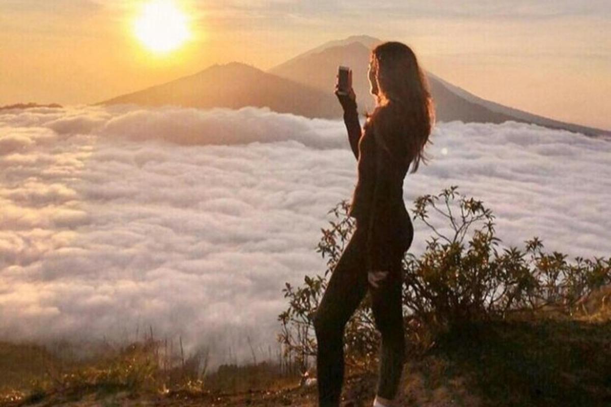 Una mujer parada en la cima de una montaña tomando una fotografía de las nubes.