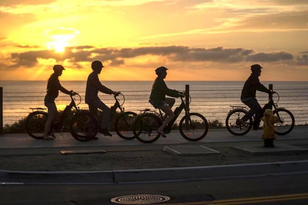a group of people riding bikes on a sidewalk near the ocean