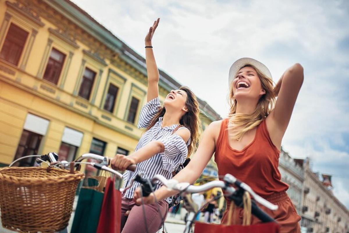 due donne che vanno in bicicletta lungo una strada con le mani in aria