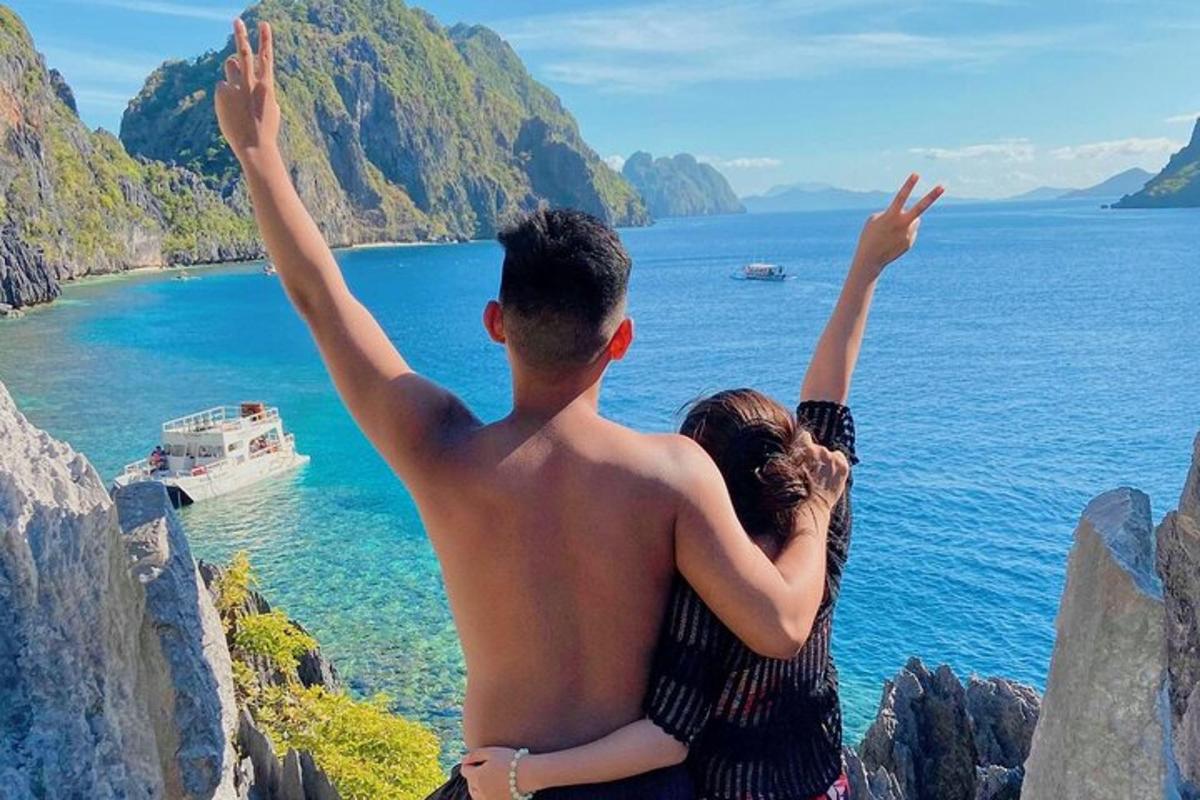 a man and a woman sitting on a cliff with their arms up