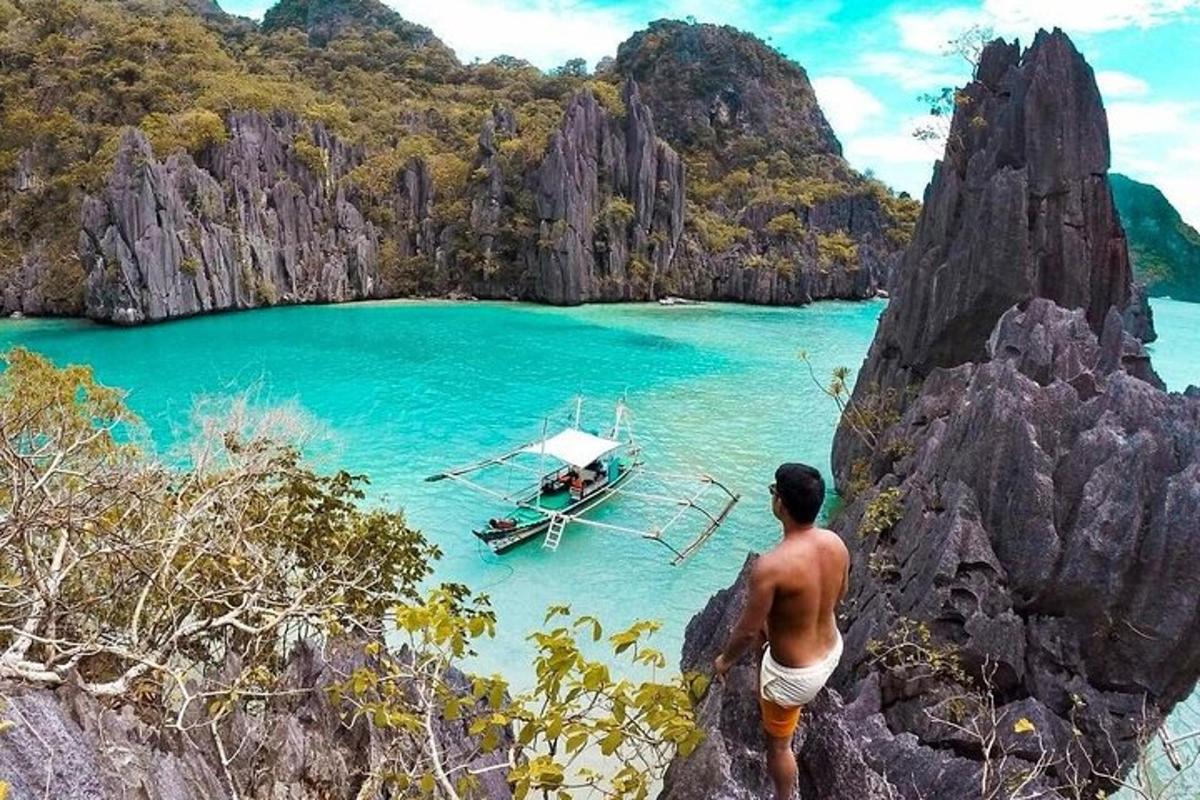 a man standing on a cliff looking at a boat in the ocean