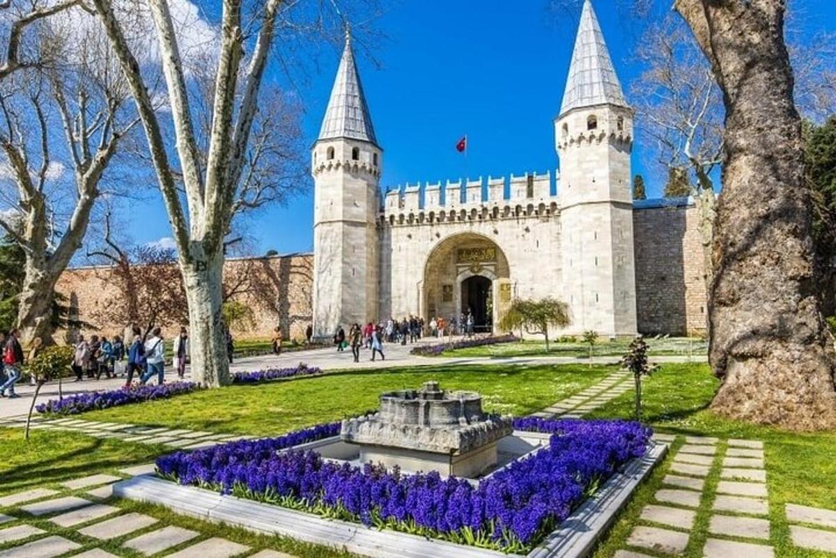 Un edificio con una fuente en un parque con flores moradas.