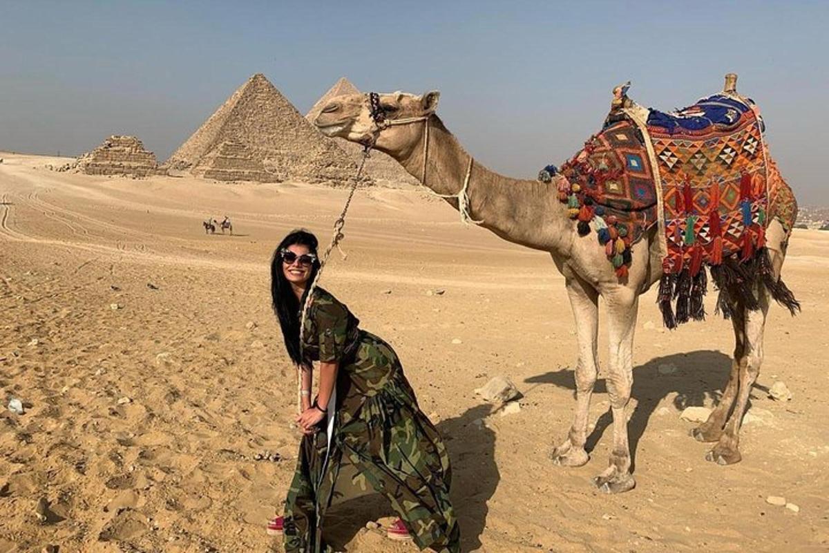 a woman standing next to a camel in front of the pyramids