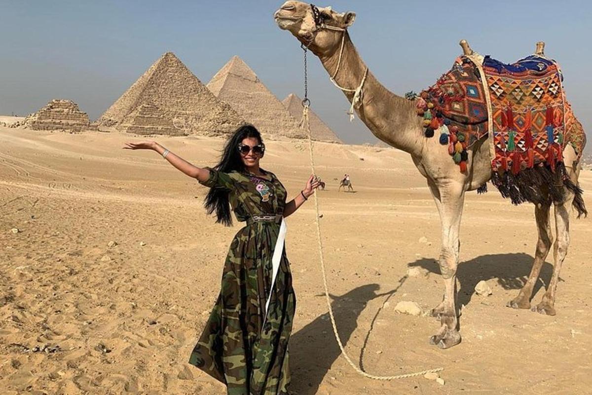 a woman standing next to a camel in front of pyramids