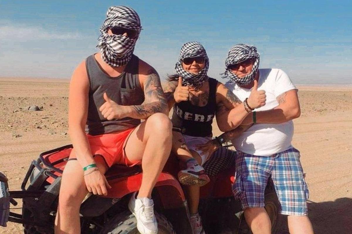 tiga orang duduk di belakang atv di padang pasir