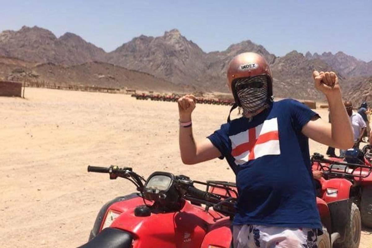 seorang lelaki memakai topi keledar dan bertopeng berdiri di sebelah motosikal