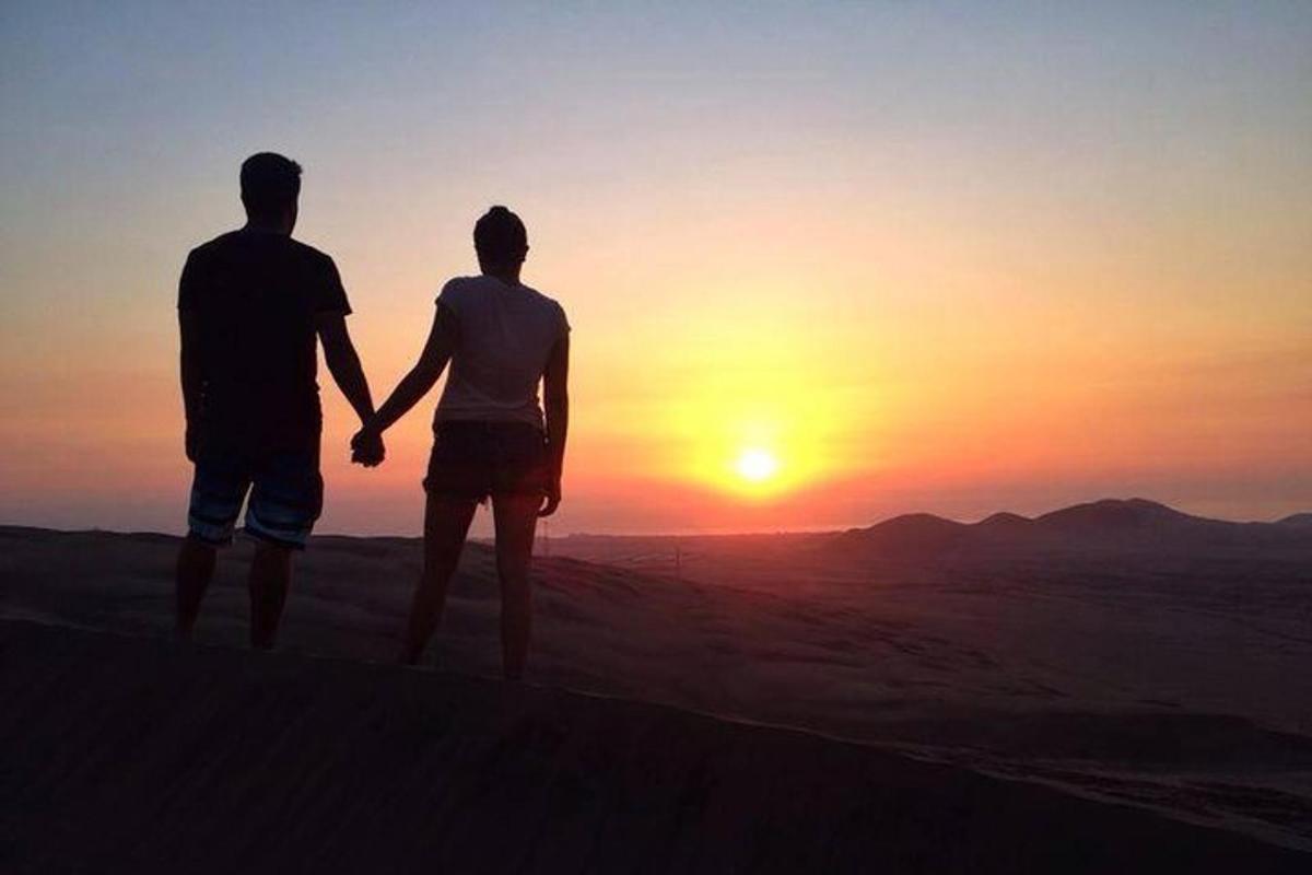 زوجان يمسكان بأيدي بعضهما أثناء وقوفهما أمام غروب الشمس