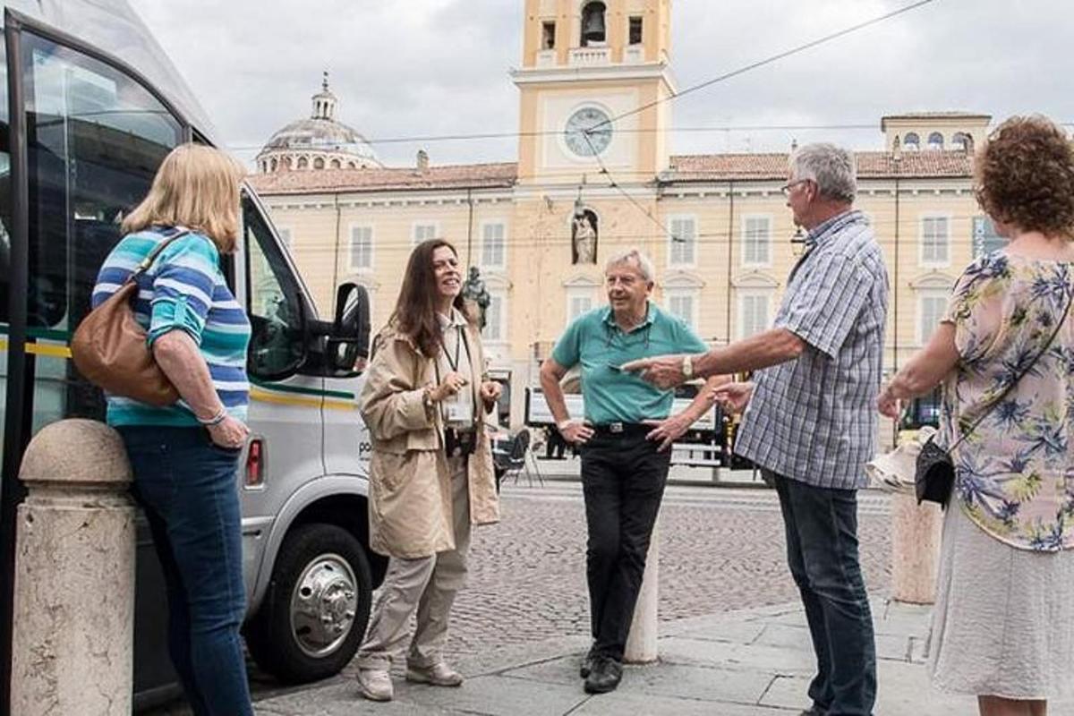 cilvēku grupa, kas stāv uz ietves pie autobusa