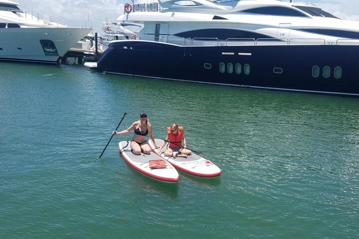 two women on a paddle board in the water next to a yacht