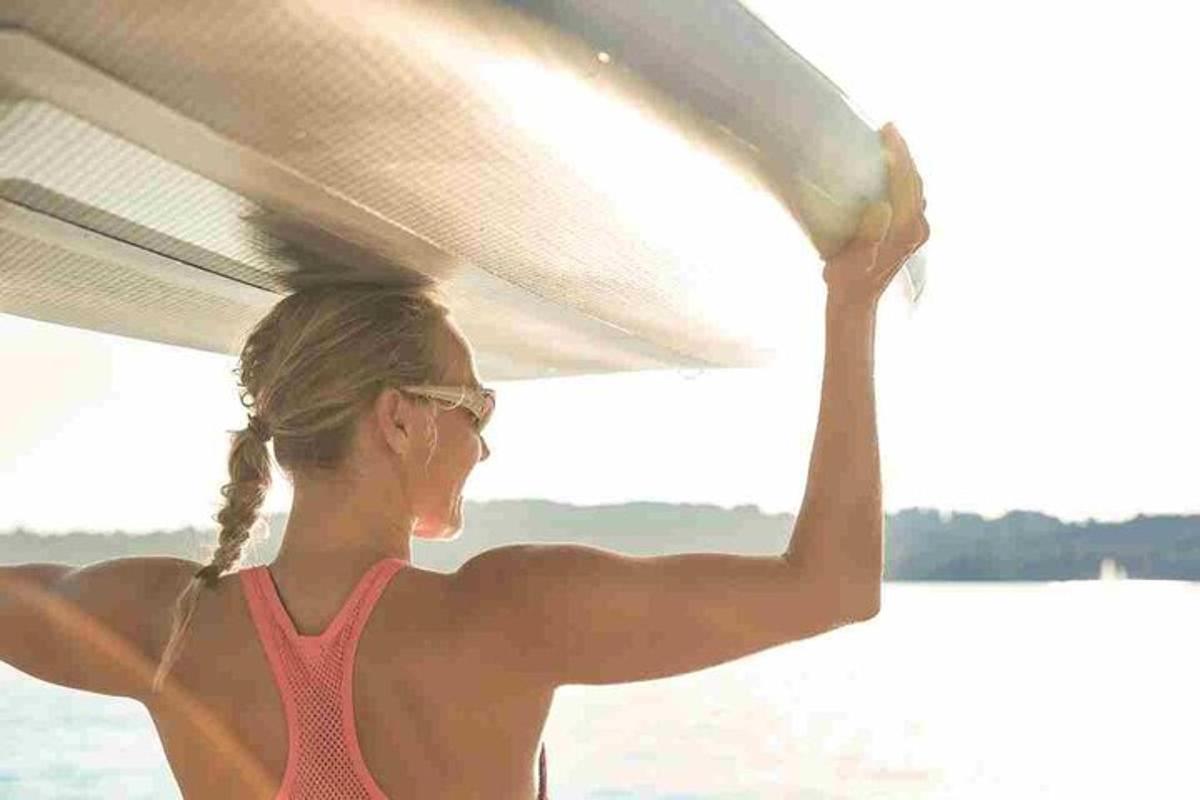 žena v bikinách nesoucí surfovací prkno na pláži