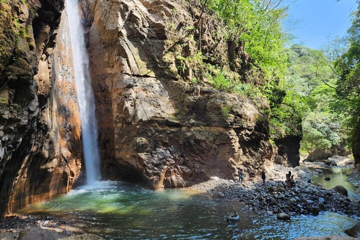 a waterfall with people standing in the water in front of it