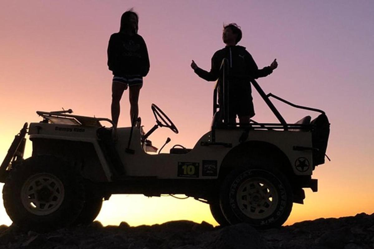 dues persones dempeus sobre un jeep a la posta de sol