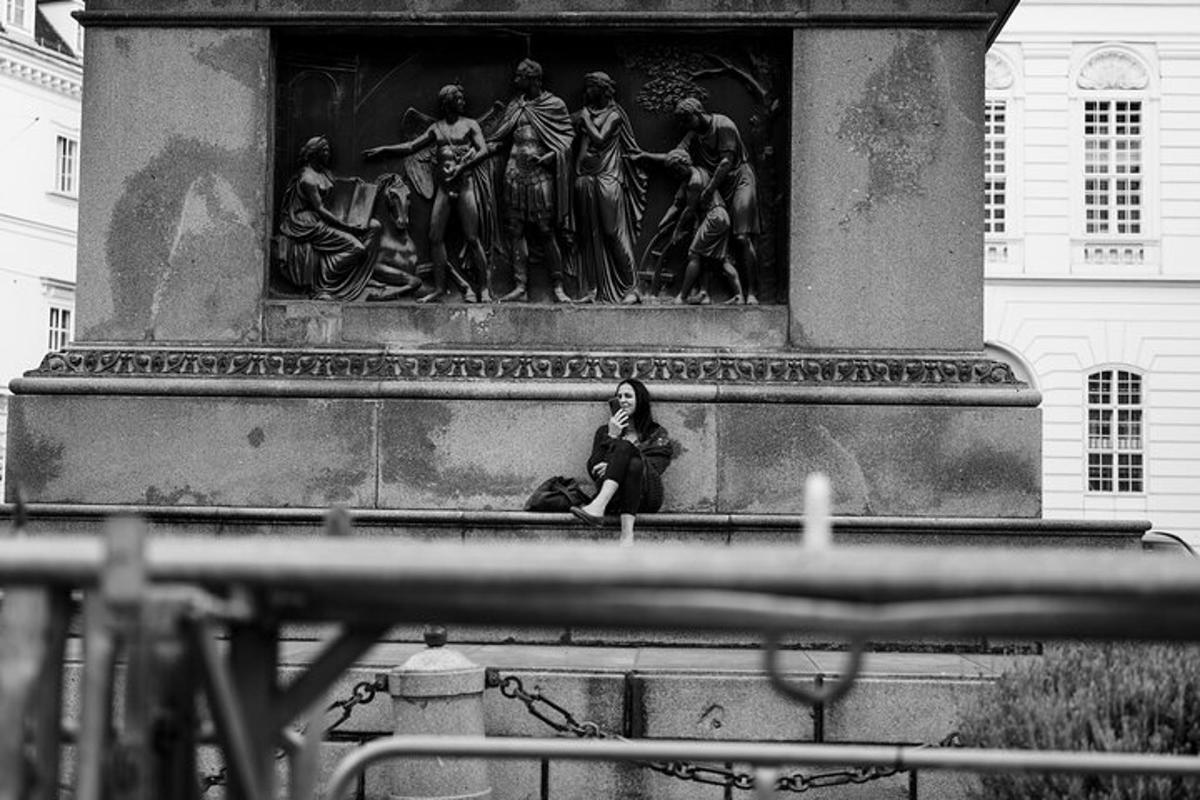 una mujer sentada en una cornisa frente a una estatua