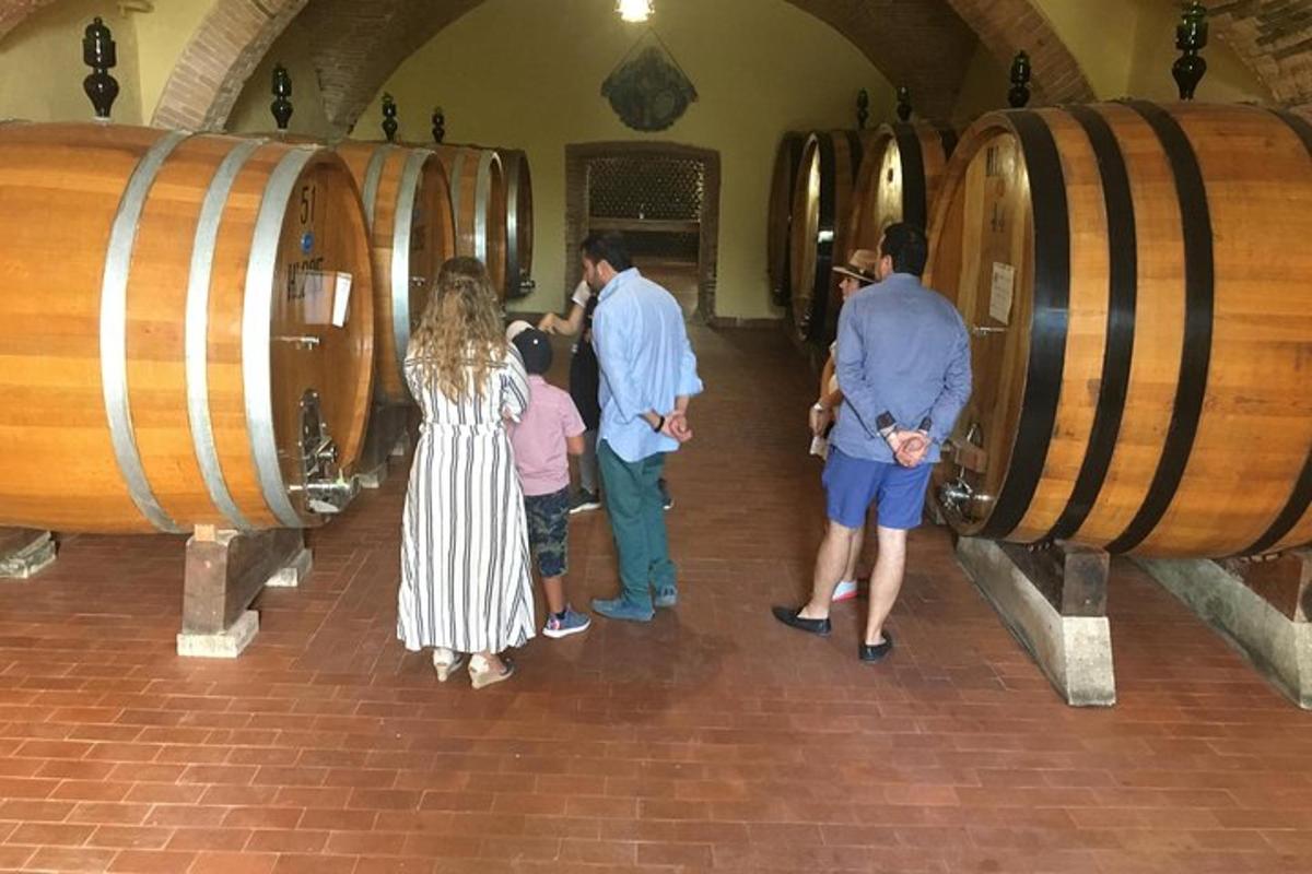 isang grupo ng mga tao na nakatayo sa isang wine cellar na may mga bariles