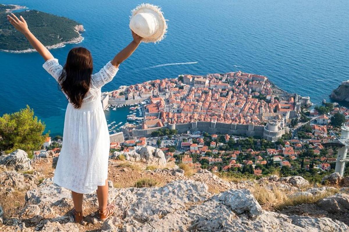 Una niña con un vestido blanco parada en la cima de una colina con los brazos en alto.