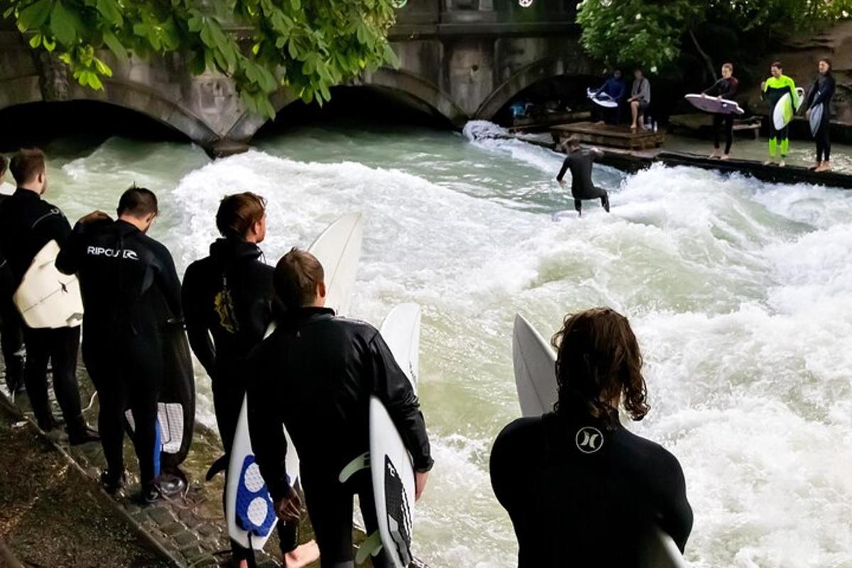 un groupe de personnes en combinaison de plongée regardant un homme surfer sur une rivière