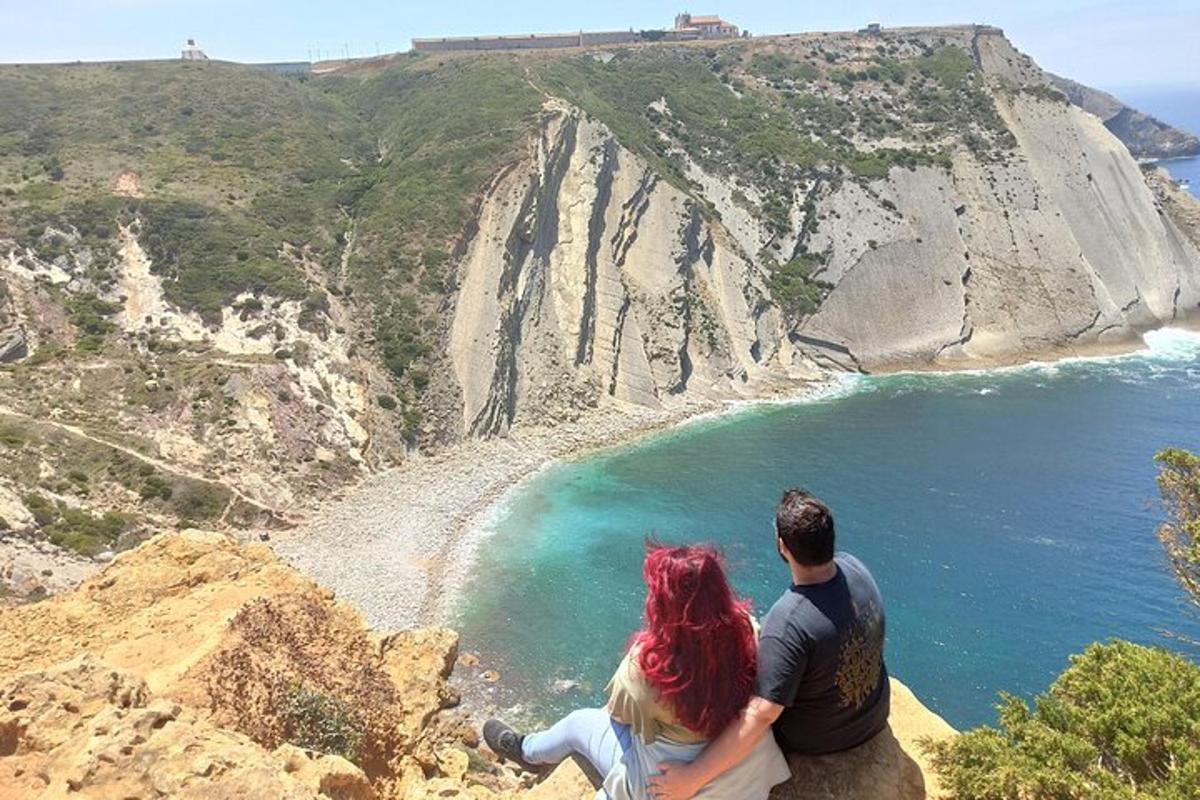 a man and a woman sitting on a rock overlooking the ocean