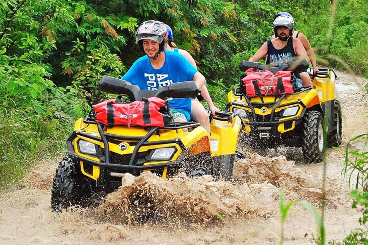 two men riding on atvs in the mud