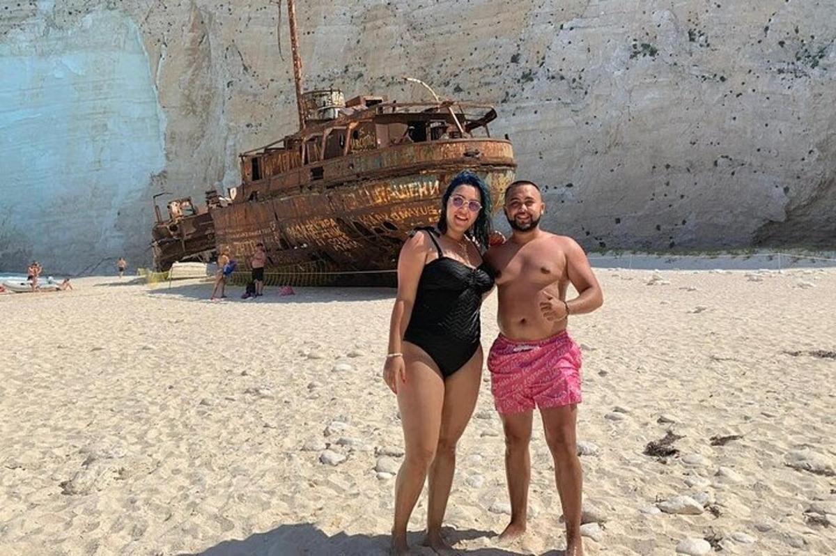 um homem e uma mulher em pé em uma praia com um navio
