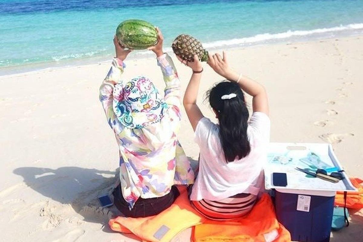 due persone sedute sulla spiaggia che tengono in mano delle angurie
