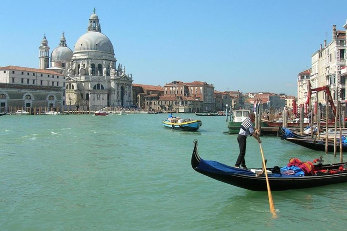 seorang lelaki sedang mendayung gondola di dalam air berhampiran sebuah bandar