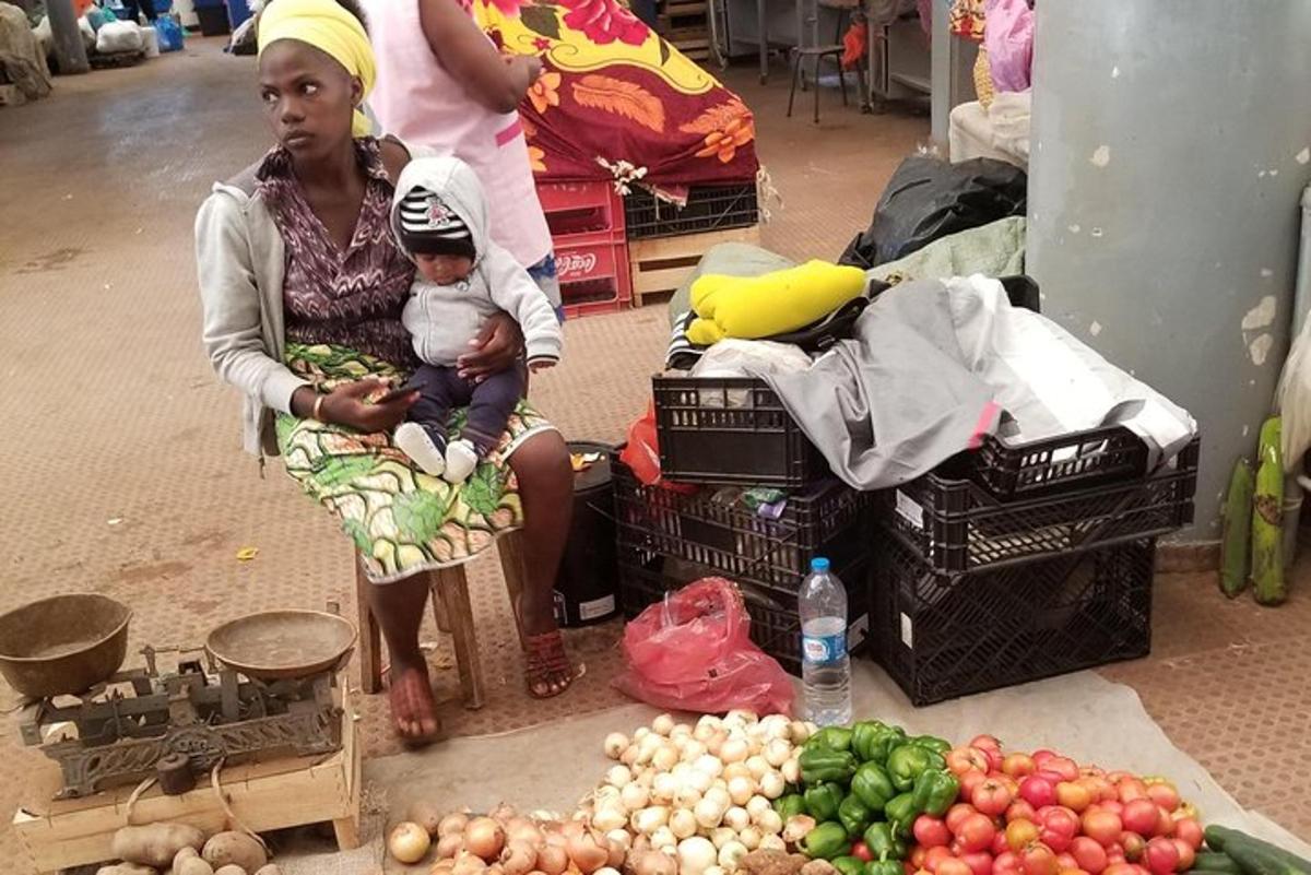 a woman holding a baby sitting next to a pile of produce