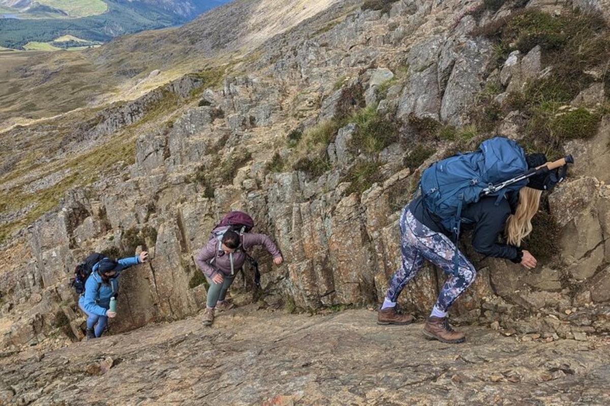 three people climbing up a rocky mountain with backpacks