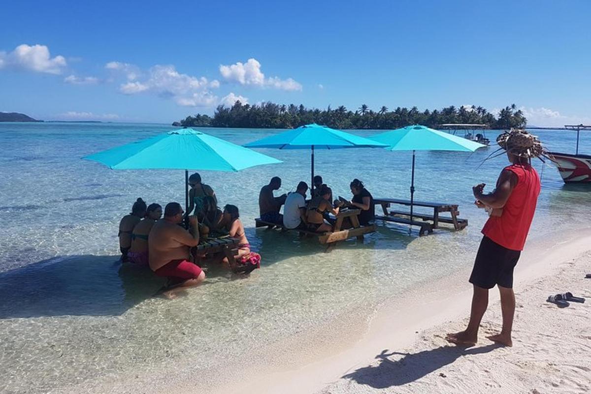 skupina ljudi, ki sedijo pod modrimi senčniki na plaži