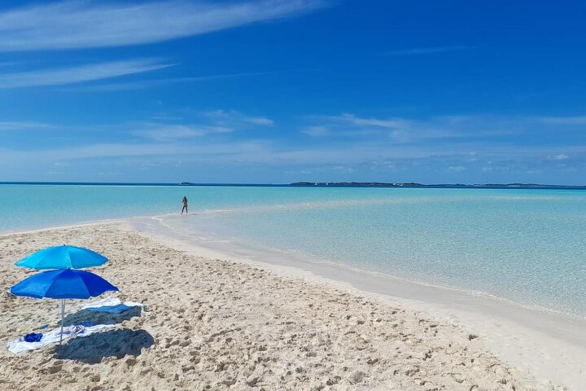 a blue umbrella on a beach with a man in the distance