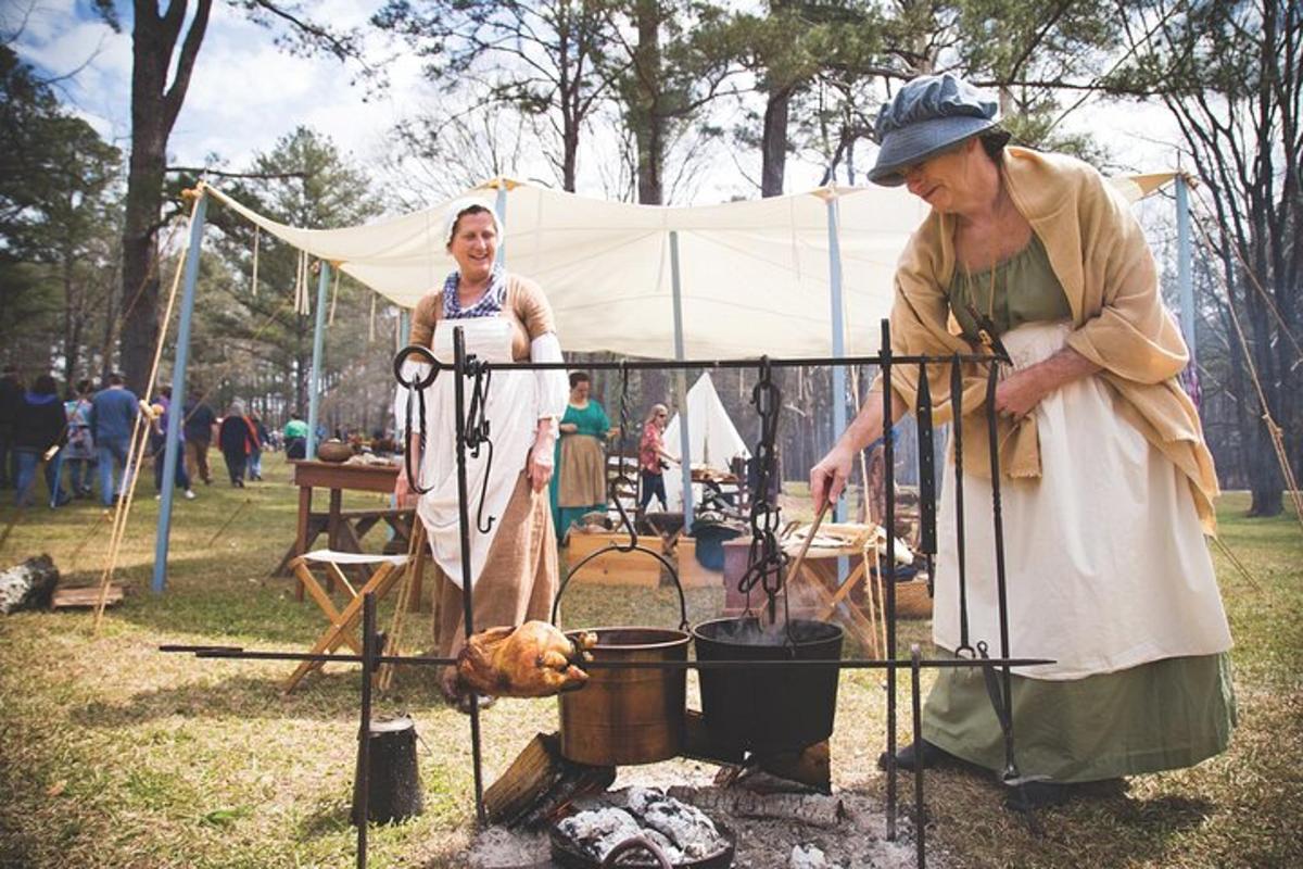 a woman standing next to a man cooking food on a grill