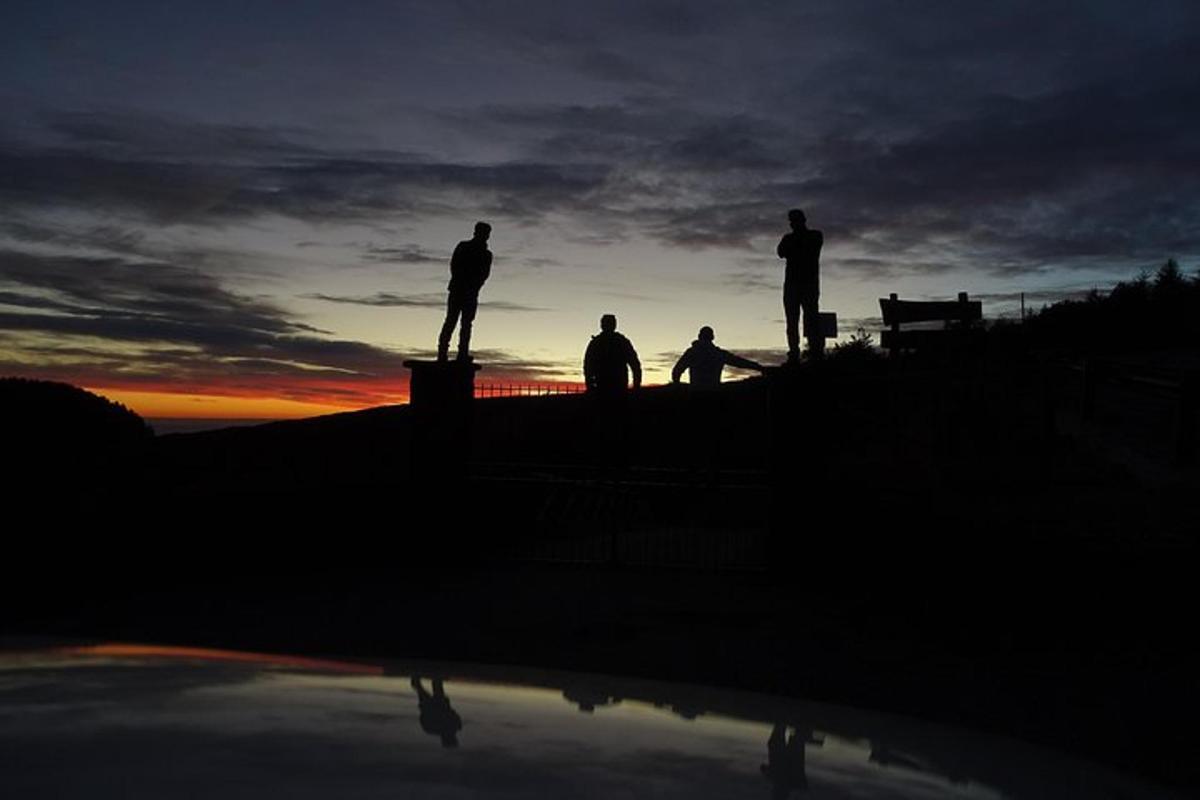 a group of three people standing on a ledge at sunset