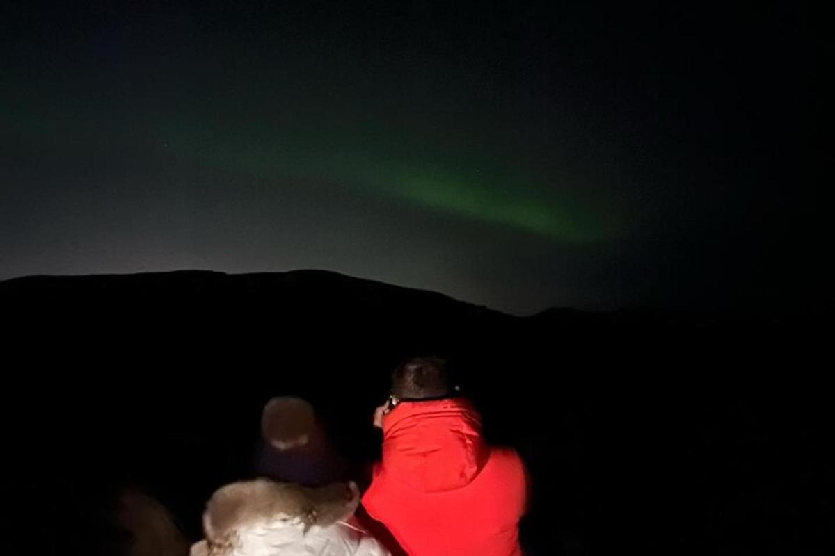 tre persone stanno guardando l'aurora boreale verde