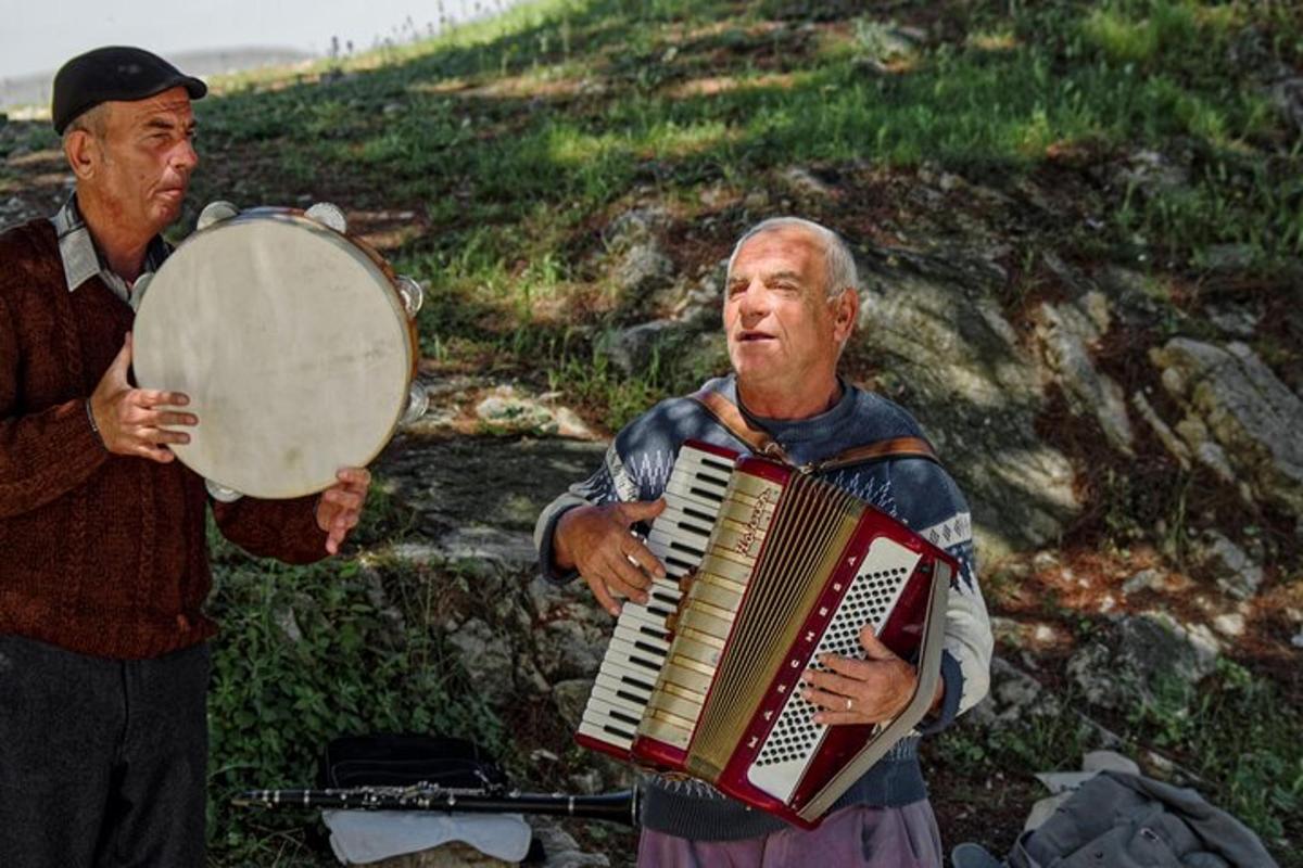 een oudere man die accordeon speelt naast een andere man