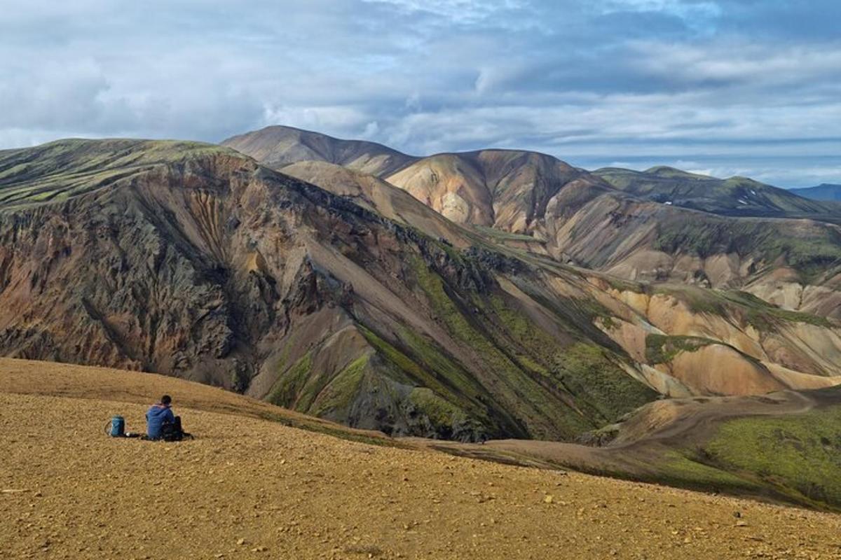 un uomo seduto su una collina che guarda una montagna