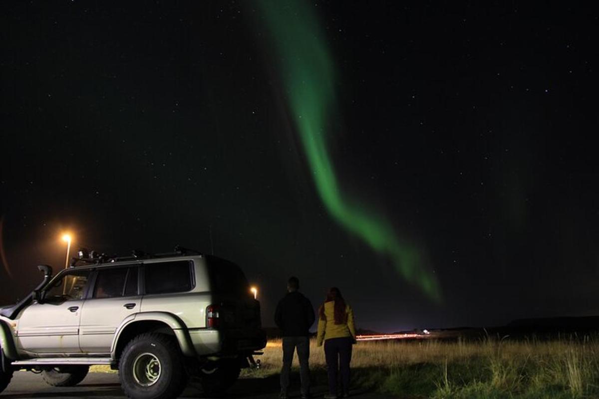 dva lidé stojící vedle bílého SUV pod polární září