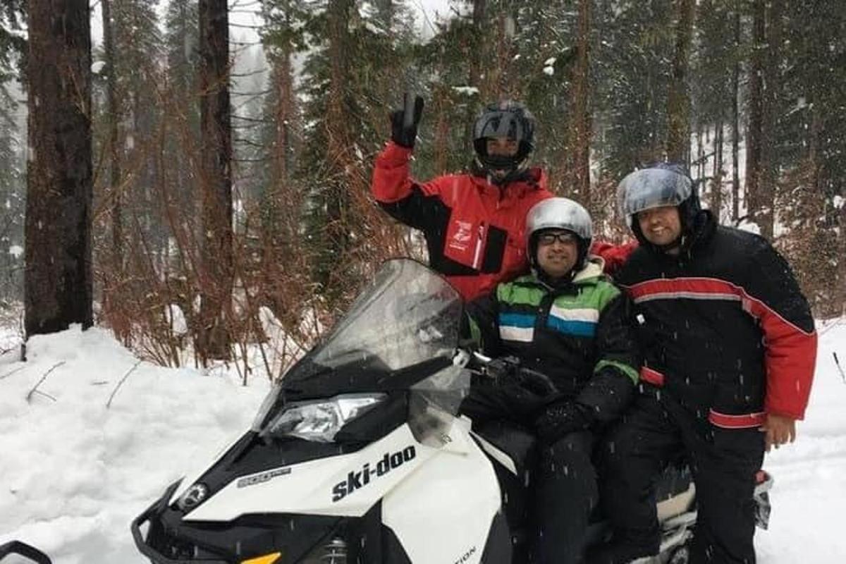 skupina treh ljudi, ki sedijo na motornih saneh