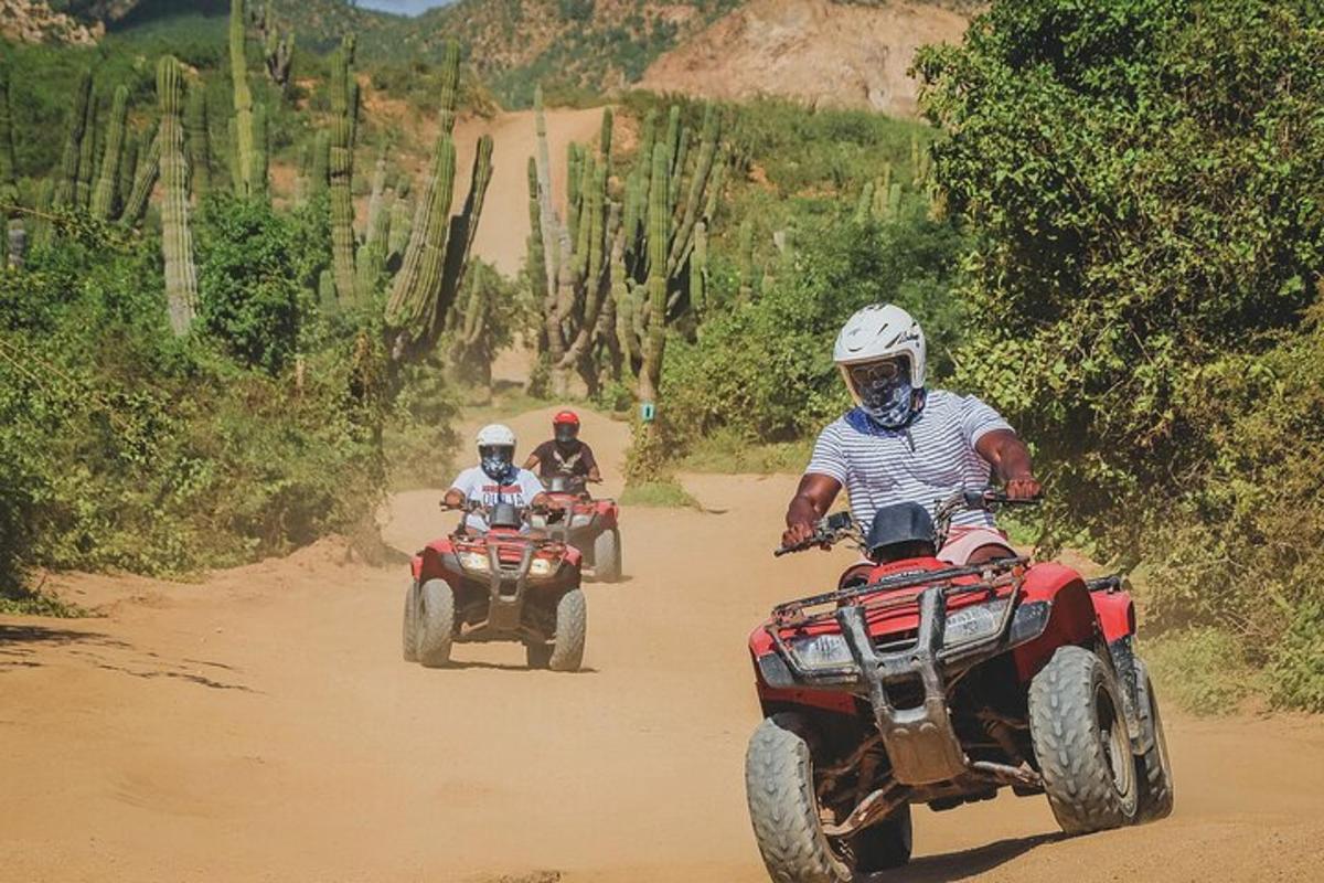two people riding on atvs on a dirt road