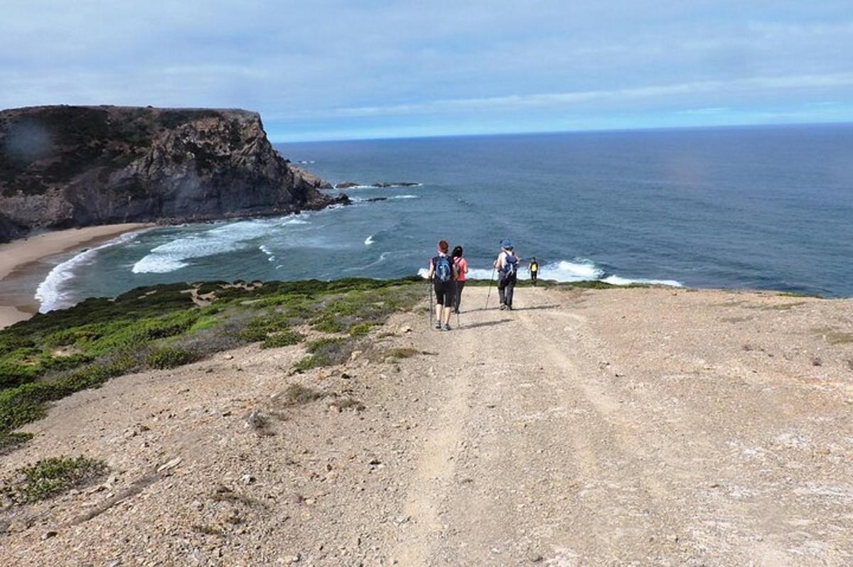 two people walking on a dirt road near the ocean