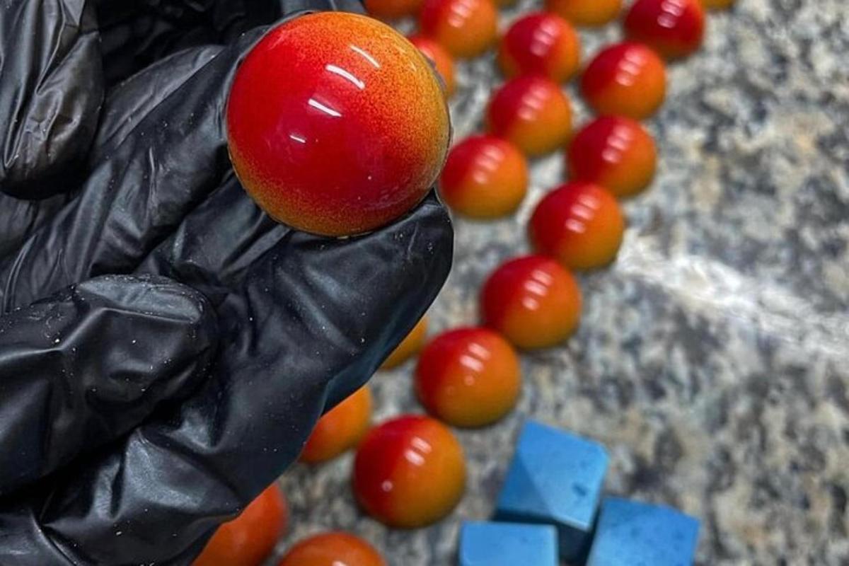 a persons hand holding a red fruit next to a bunch of tomatoes