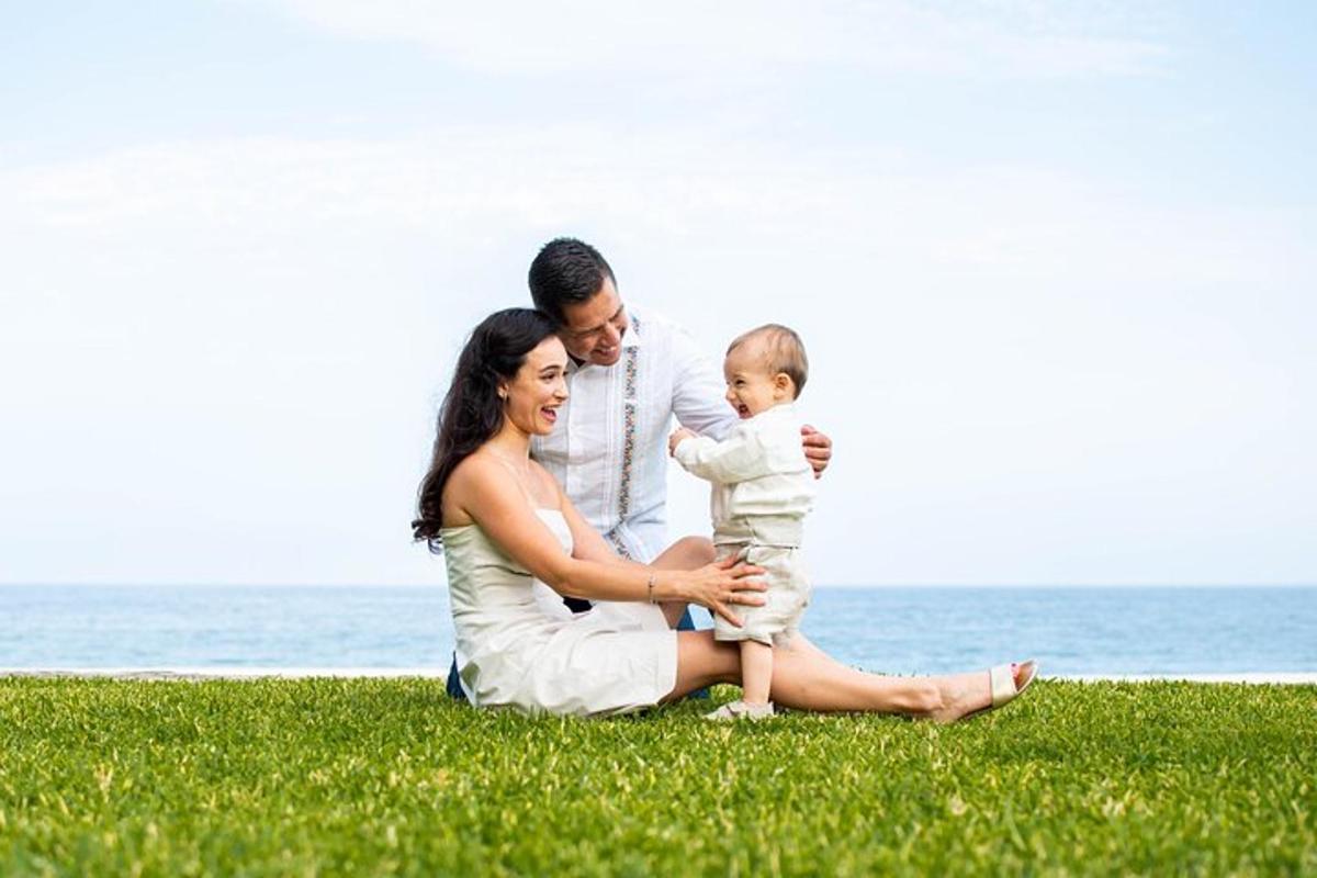 a woman and man holding a baby sitting on the grass