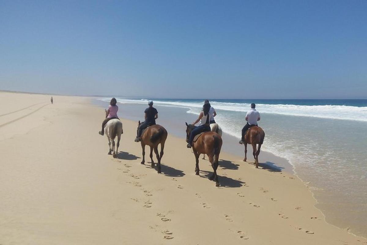 un grup de persones muntant a cavall a la platja