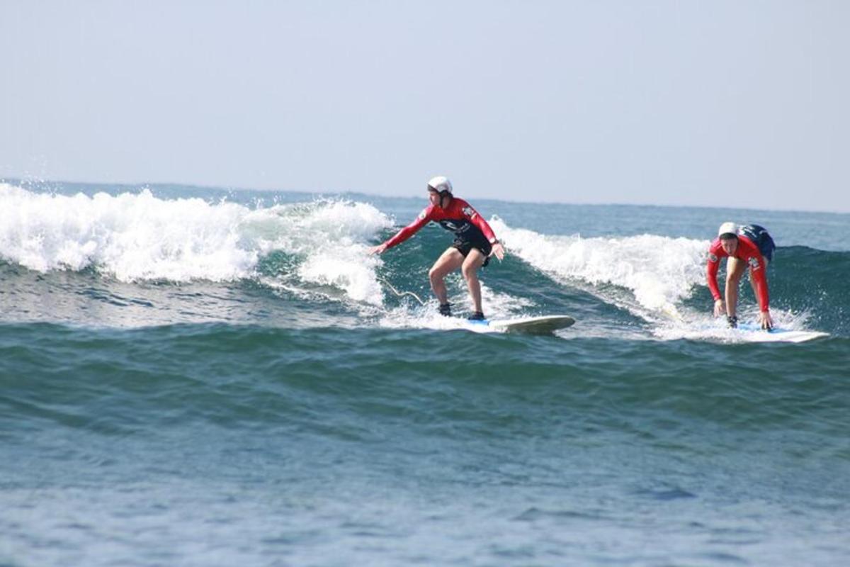 Două persoane călărind un val pe plăci de surf în ocean